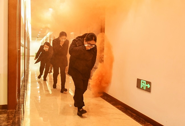 图为：演练模拟办公区起火，火势蔓延并产生浓烟，参训人员低姿弯腰、湿毛巾捂口鼻，沿预定通道快速撤离2.jpg